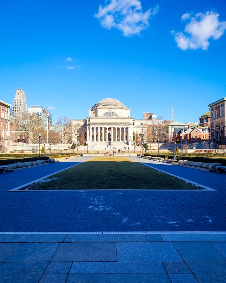 Columbia University New York City USA Non-Touristy Activities for Return Visitors to New York City A large shadowed area on the Columbia University campus in New York City, USA. There's a big grass area with a path around it and behind that is a large stone building with a big dome on top. Around it are more buildings and above is the blue sky "Non-Touristy Activities for Return Visitors to New York City"