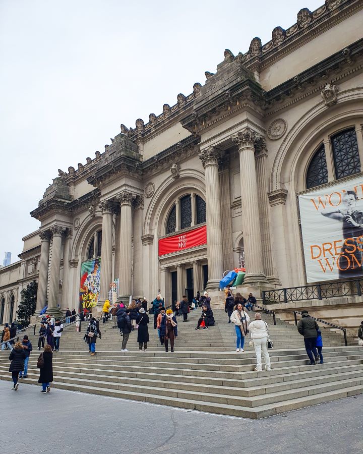 Met Museum New York City USA Non-Touristy Activities for Return Visitors to New York City The Met museum in New York City, USA. It's a big beige building with 6 columns out the front and a fancy roof. There's also three big arched windows on the front and stone steps leading up to the doors with people all over the stairs "Non-Touristy Activities for Return Visitors to New York City"