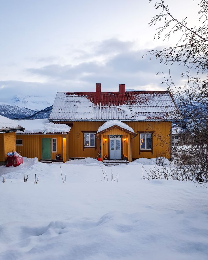 Northern Lights in Tromsø: Why It's the Best Place To Be Our Airbnb in Tromsø, Norway. It's a little yellow wooden house with a red roof and it has a front yard that is covered in thick snow. "Northern Lights in Tromsø: Why It's the Best Place To Be"
