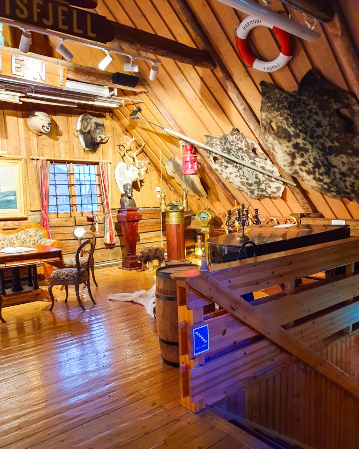 Best Things To Do in the City of Tromsø, Norway Inside the Polar Museum in Tromsø, Norway. It's all made of wood with a wooden floor, slanted roof and staircase. On the walls are some animal rugs and heads stuck to the wall and there's furniture around too. "Best Things To Do in the City of Tromsø, Norway"