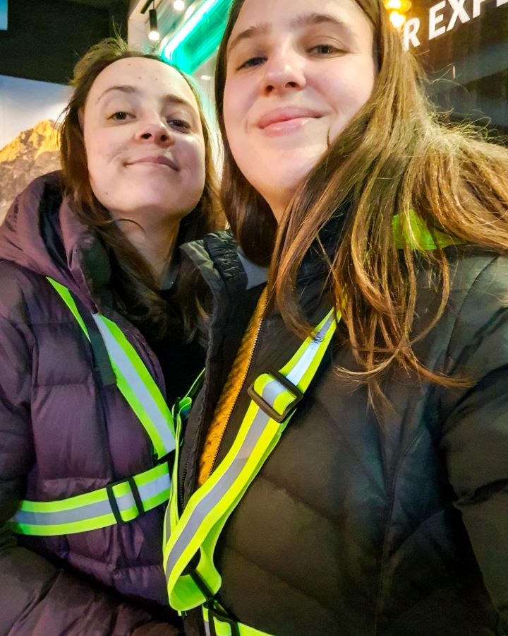 Northern Lights in Tromsø: Why It's the Best Place To Be Krissie and Katherine looking at the camera about to go on a tour in Tromsø, Norway. They're wearing puffer jackets with fluro straps over the top so they can be seen in the dark. "Northern Lights in Tromsø: Why It's the Best Place To Be"