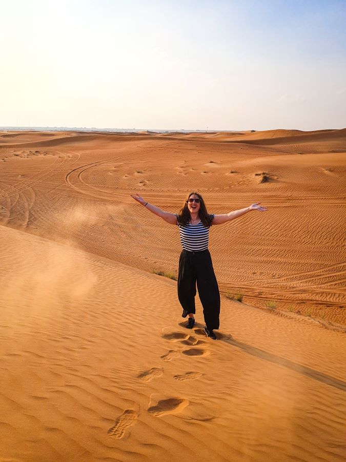 Katherine standing in the Arabian Desert, UAE and her hands are up after throwing some sand up in the air. "Dubai Desert Safari Experience: Detailed Get Your Guide Review"