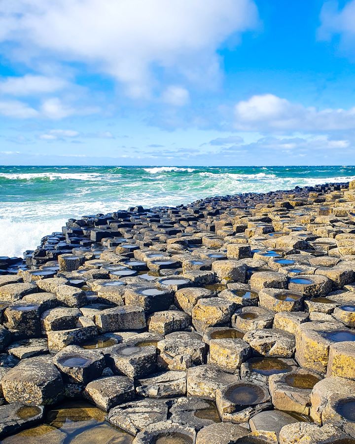 Lots of hexagonal rocks with the ocean behind them at the Giant's Causeway, Northern Ireland. The rocks have worn down in the middle so there's pools of water in the middle of a lot of them. "Giant's Causeway from Belfast: Get Your Guide Review"