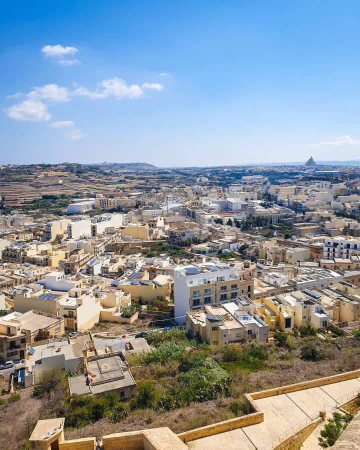 Victoria Citadel Malta Explore Gozo and the Blue Lagoon in Malta: Detailed Get Your Guide Review A view over Gozo, Malta from the Citadel. There's heaps of yellow and white buildings with brown land and green bushes around. Above it all is a blue sky with some clouds. "Explore Gozo and the Blue Lagoon in Malta: Detailed Get Your Guide Review"