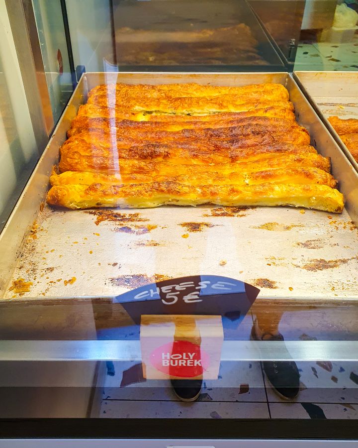 A metal tray with rolls of crispy pastry burek in Dubrovnik, Croatia. There's a sign in front that says cheese 5 euros and another one that says "Holy Burek". "How to Spend Three Days in Dubrovnik: Best Itinerary For a First Visit"