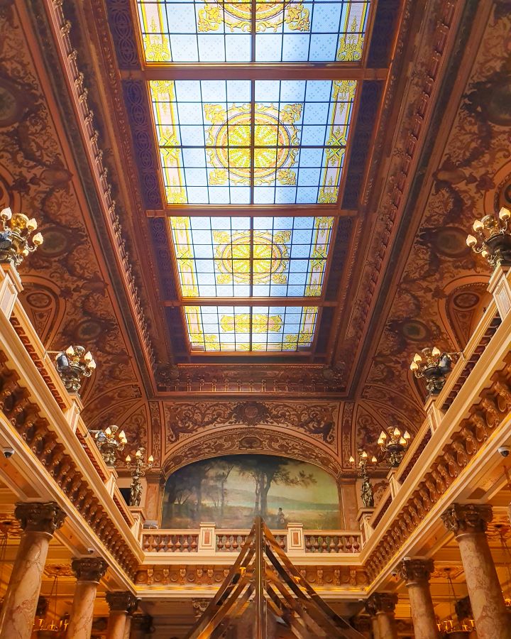 Inside the Monte-Carlo casino entry hall in Monaco. The walls and roof are all a deep orange colour with carvings and the roof is a glass skylight with patterns in it too. "The Best Budget Nice to Monaco Day Trip"