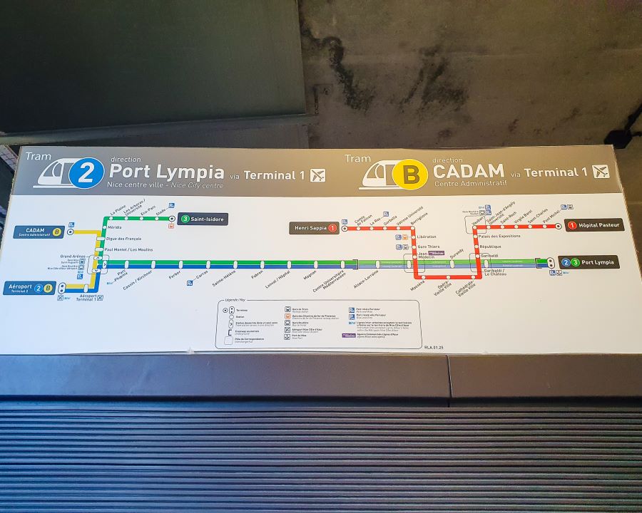 A sign of the tram system in Nice, France. There's different lines in red, green, blue and yellow with lots of different stops along them and the sign is in both French and English. How to Navigate Public Transport in and Around Nice, France