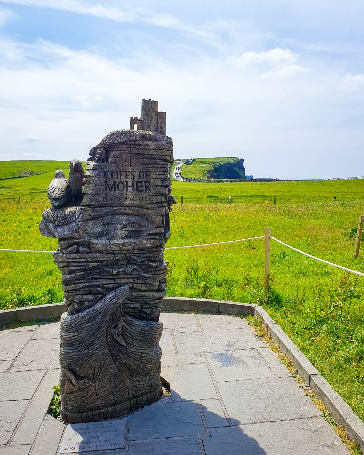 Ireland Cliffs of Moher From Galway: Get Your Guide Review A wooden statue saying Cliffs of Moher experience on it in Ireland. Behind it is green grass and you can see the edge of a cliff. Cliffs of Moher From Galway: Get Your Guide Review