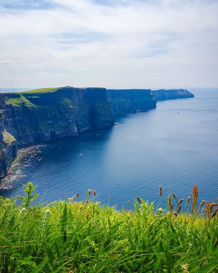 Ireland Cliffs of Moher From Galway: Get Your Guide Review Looking at the cliffs of Moher, Ireland. In the foreground is green grass and behind is a view of the sprawling cliffs. They're dark grey with green grass on top and the water on the right is dark blue. Cliffs of Moher From Galway: Get Your Guide Review
