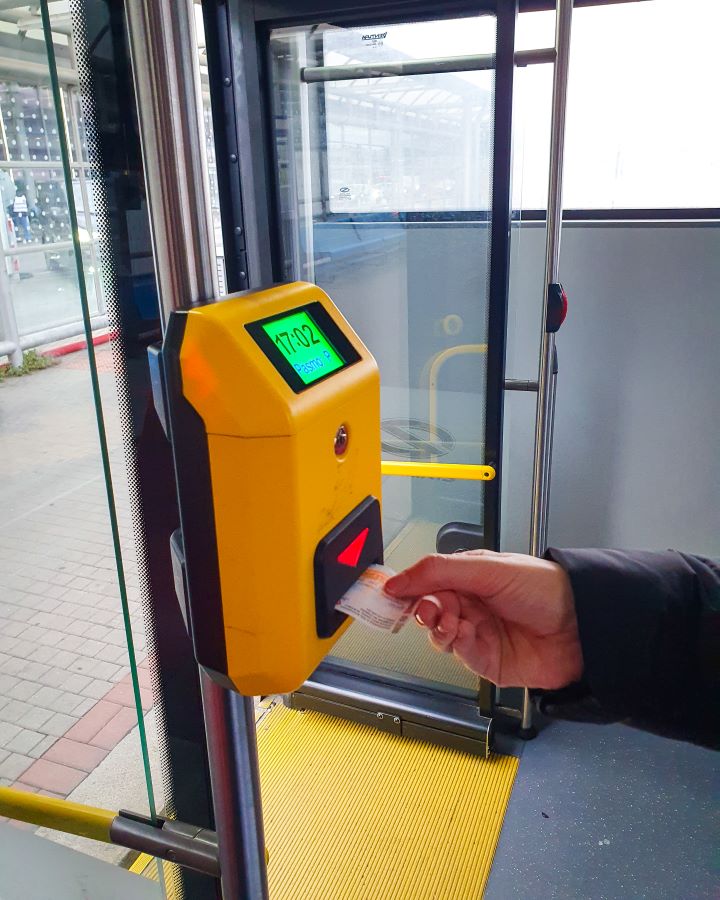 Prague Czechia A Complete Guide to Prague Public Transport A hand putting a little ticket into a yellow validation machine. The person is on a tram so the tram doors are behind them waiting at a stop in Prague, Czechia. A Complete Guide to Prague Public Transport