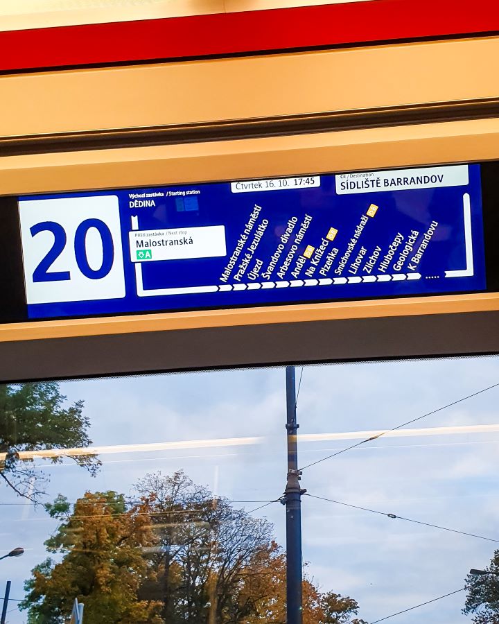 Prague Czechia A Complete Guide to Prague Public Transport An electronic list of tram stops on a tram in Prague, Czechia. There's a number 20 on the left (the tram number), with a line of stops so you know where you are next to it. Under the sign is a window with some trees outside. A Complete Guide to Prague Public Transport