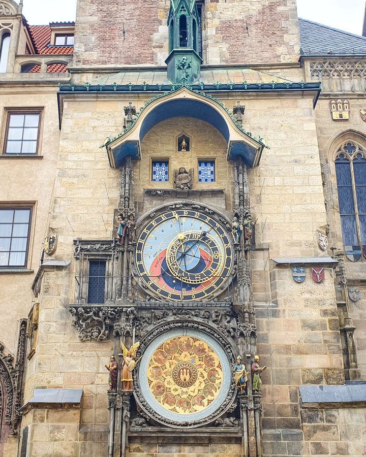 The Prague clock with two circles, the top one with a big clock face on it. It's on the side of a sand coloured building and it has lots of gold on it. How To Visit Prague On a Budget: Best Three Day Itinerary