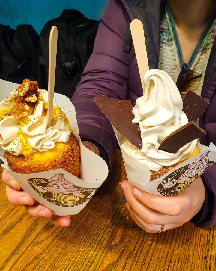 Krissie holding two chimney cakes in Prague, Czechia. One has soft serve and chocolate pieces in it and one has cream, walnuts and honey on it. How To Visit Prague On a Budget: Best Three Day Itinerary