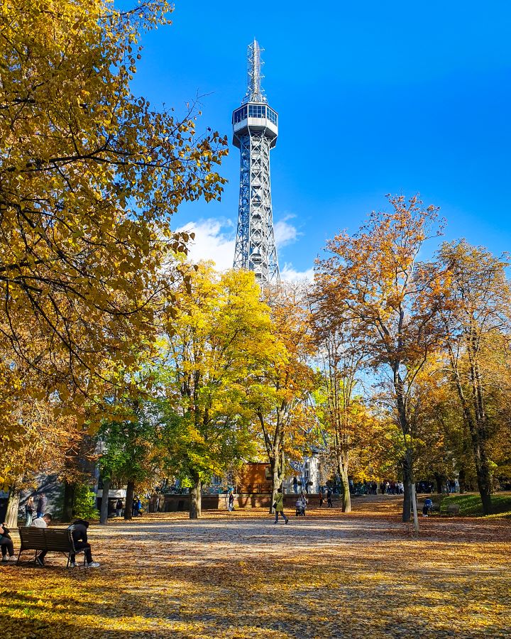 Petřín tower on Petřín Hill in Prague, Czechia. The tower looks like a small Eiffel tower and there's yellow trees in front if it with leaves all over the ground. How To Visit Prague On a Budget: Best Three Day Itinerary