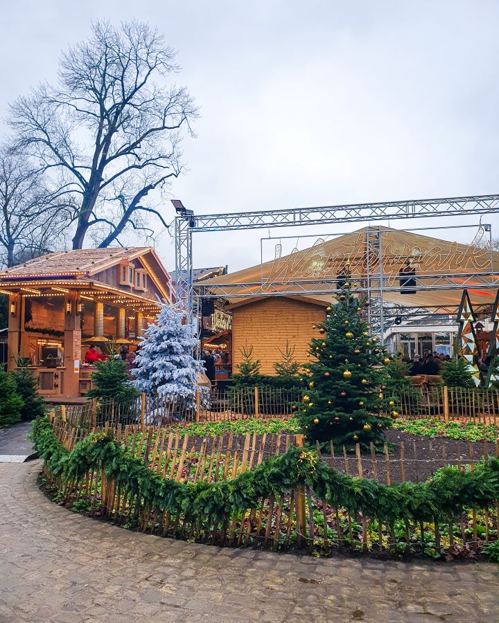 A Christmas market in Luxembourg City. There's Christmas trees outside with some wooden huts behind them. It's during the day so it's light outside. Make the Most of Christmas in Luxembourg City