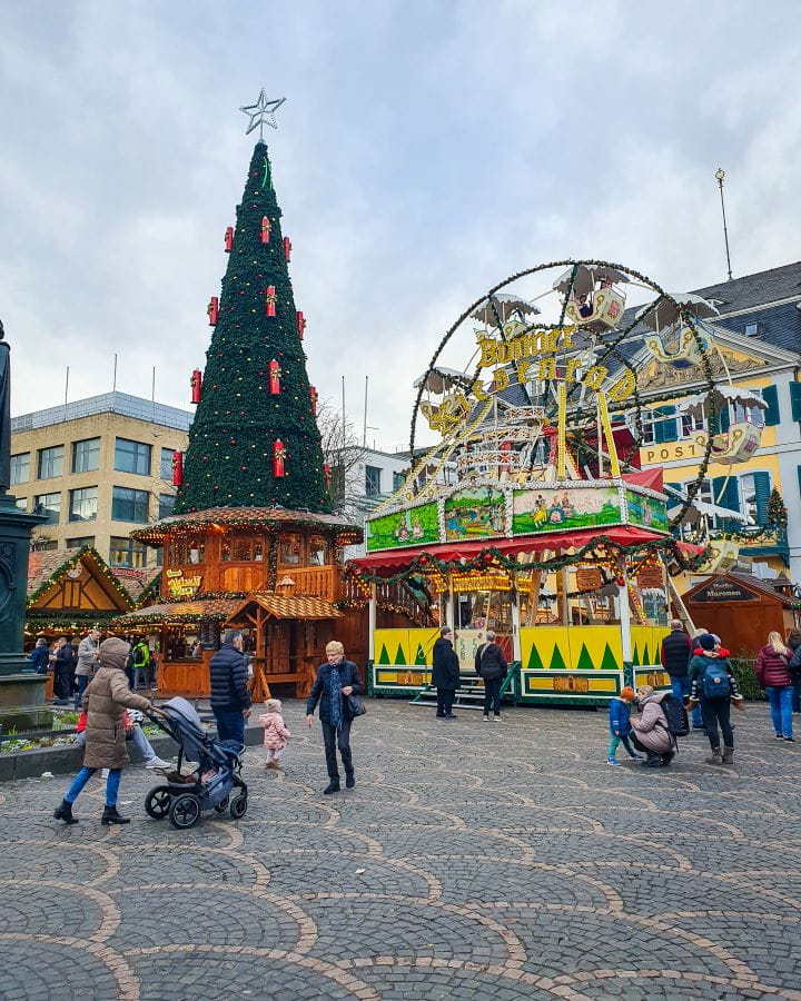 Münsterplatz Bonn Germany How To Make The Most of a Day in Bonn from Cologne A square in Bonn, Germany with a Christmas market in it. There's people walking around with a small Ferris wheel, a large fake Christmas tree and some wooden huts around. How To Make The Most of a Day in Bonn from Cologne