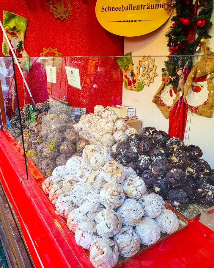 Schneeballs Münsterplatz Bonn Germany How To Make The Most of a Day in Bonn from Cologne A stall with stacks of fried balls of dough on a red table in Bonn, Germany. The balls are different colours, some are covered in chocolate and behind it is a sign that says "Schneeballenträume" on it. How To Make The Most of a Day in Bonn from Cologne