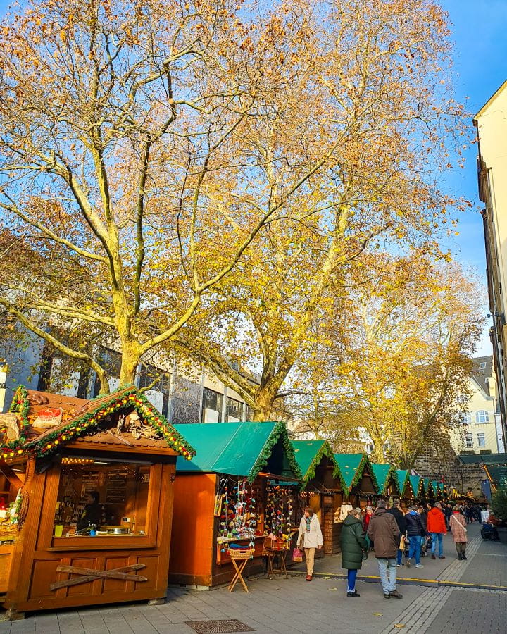 Bottlerplatz Bonn Germany How To Make The Most of a Day in Bonn from Cologne Little wooden huts with green roofs in a square in Bonn, Germany. There's tree's and buildings behind the huts and people walking around looking at the market. How To Make The Most of a Day in Bonn from Cologne