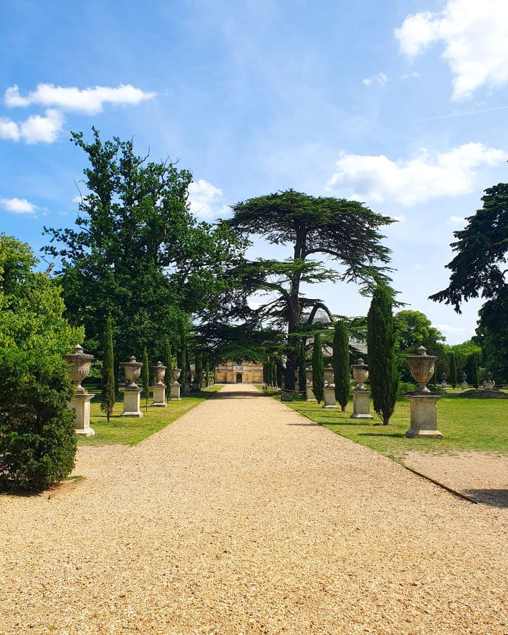 Chiswick House and Gardens London Less Touristy Places in London for Return Visitors A pebbly path leading up to a stone house in Chiswick Gardens, London. Around the path are stone vases, trees and green grass. Less Touristy Places in London for Return Visitors