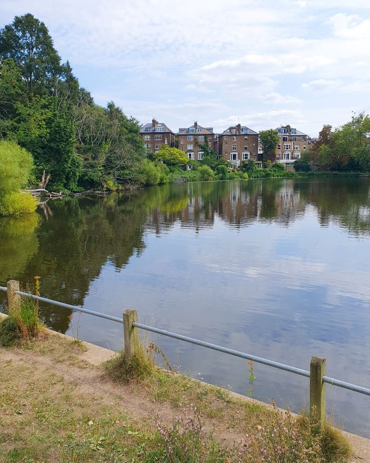 Hampstead Heath London Less Touristy Places in London for Return Visitors A bigger clear lake with trees at the back and 4 big stone houses behind the trees looking out onto the lake. Less Touristy Places in London for Return Visitors