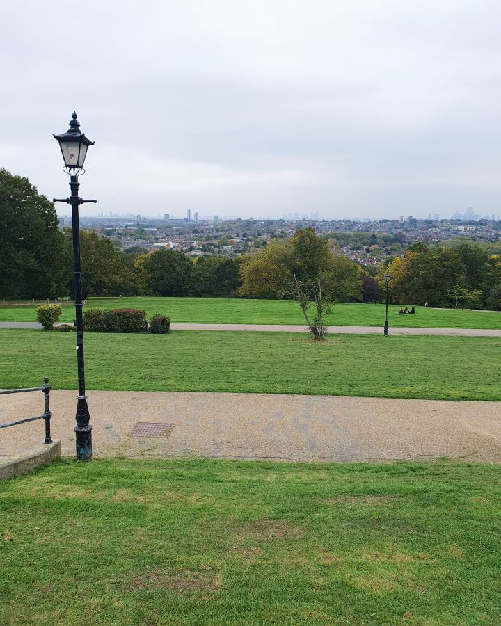 Alexandra Park London Less Touristy Places in London for Return Visitors A hill in Alexandra Park with a view back to London. The grass is green with paths going across it and there's green trees on the hill as well as some black lamp posts. Less Touristy Places in London for Return Visitors