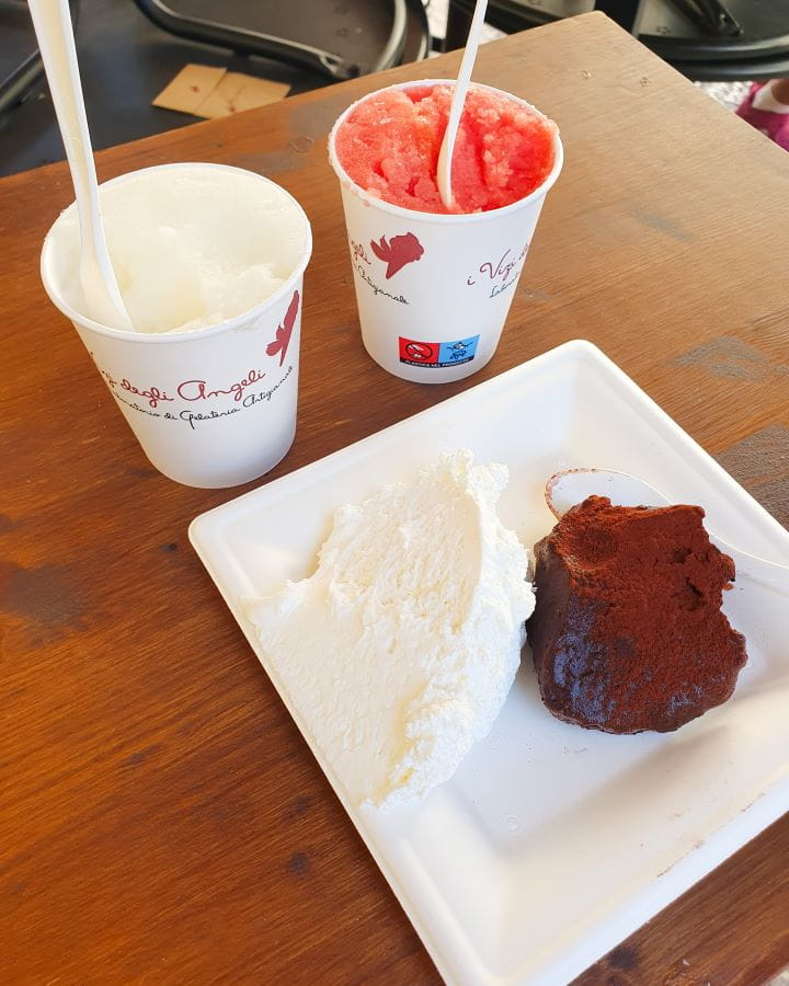 Matera Italy Three Unique Day Trips From Bari Without a Car Two cups of granita from a gelateria in Matera, Italy. One cup has white granita and one cup has pink granita and there's a white plate with a chocolate truffle and some whipped cream on it too. Three Unique Day Trips From Bari Without a Car