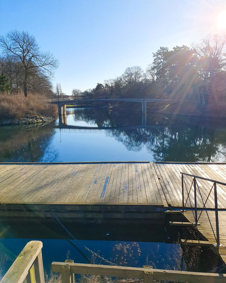 Sweden How To Have The Best Day In Malmö From Copenhagen A wooden walkway on a pond in a park in Malmö, Sweden. Behind it is more water and a bridge going over it with trees and bushes on either side. How To Have The Best Day In Malmö From Copenhagen