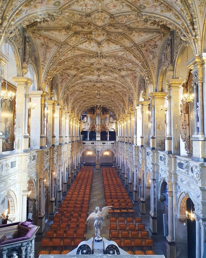 Denmark Explore Frederiksborg Castle In a Beautiful Day Trip from Copenhagen Inside the chapel in Frederiksborg castle, Denmark. In the middle are rows of red chairs and on either side are archways leading to other parts of the chapel. Above them are more archways and the domed roof above is gold and silver. There's also a big organ at the far end. Explore Frederiksborg Castle In a Beautiful Day Trip from Copenhagen