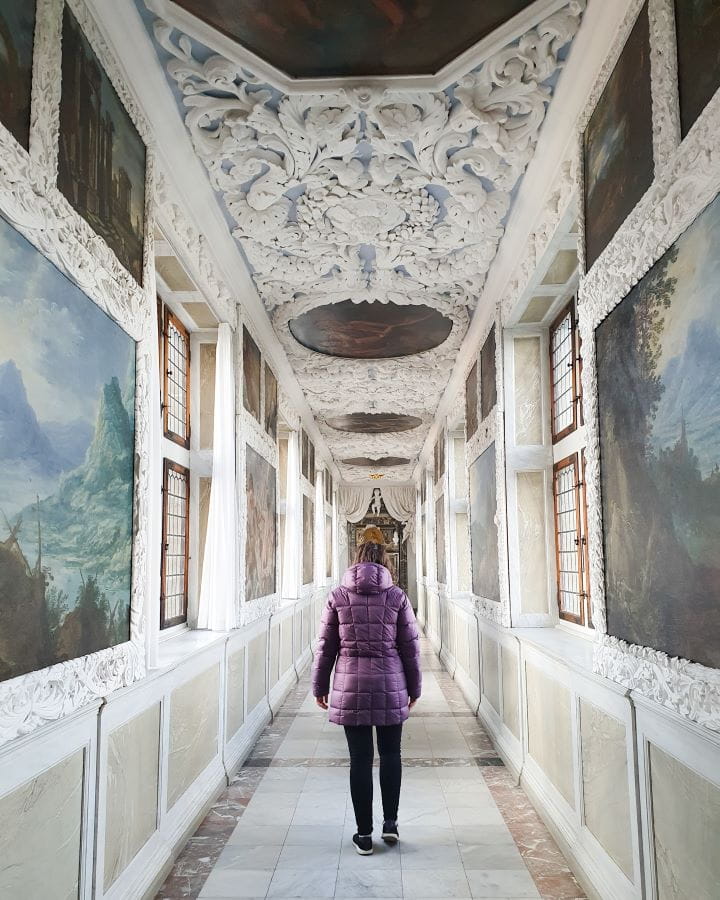 Denmark Explore Frederiksborg Castle In a Beautiful Day Trip from Copenhagen Krissie standing in a thin hallway in Frederiksborg castle, Denmark. The floor, walls and roof are white with paintings on the wall and decoration on the roof. Explore Frederiksborg Castle In a Beautiful Day Trip from Copenhagen