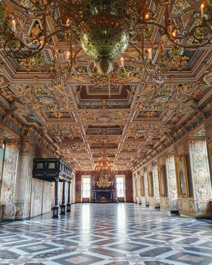 Denmark Explore Frederiksborg Castle In a Beautiful Day Trip from Copenhagen In a grand hall in Frederiksborg castle, Denmark. The floor is white and black tile and the walls and roof are gold. The roof is textured and there's a couple of chandeliers too. Explore Frederiksborg Castle In a Beautiful Day Trip from Copenhagen