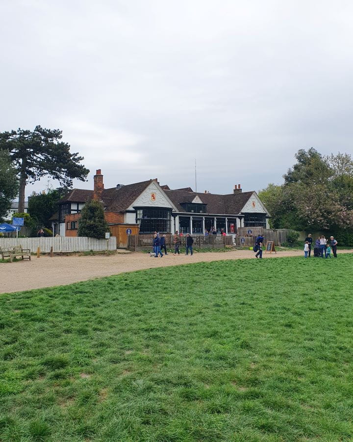 United Kingdom The Windmill tearooms Wimbledon and Putney Commons Nine Less Touristy But Wonderful Parks to Visit in London Some grass in the foreground with a café behind it in Wimbledon and Putney Commons in London. There's a dirt path between the café and the grass with people walking on it and the sky above is grey and cloudy. Nine Less Touristy But Wonderful Parks to Visit in London