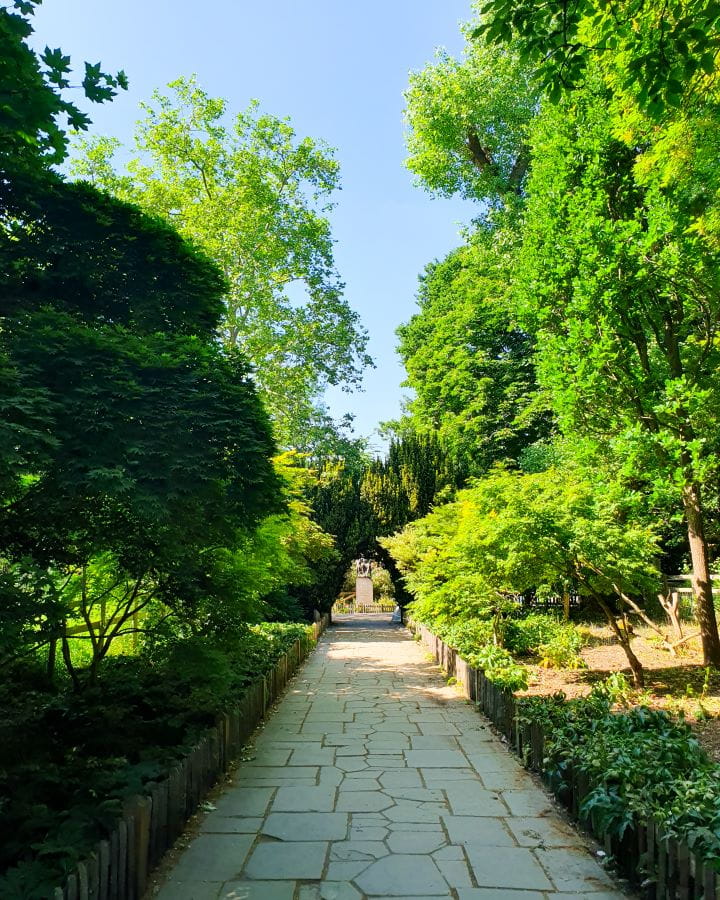 United Kingdom Holland Park Nine Less Touristy But Wonderful Parks to Visit in London A white cobblestone path going away from the camera with a little fence on either side in Holland Park, London. There's green trees on either side and it makes a little archway over the path at the end. Nine Less Touristy But Wonderful Parks to Visit in London